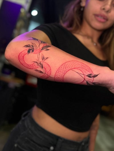 A minimal linework tattoo of a snake intertwined with leaves on the forearm, using red and black ink — by zealous, los angeles