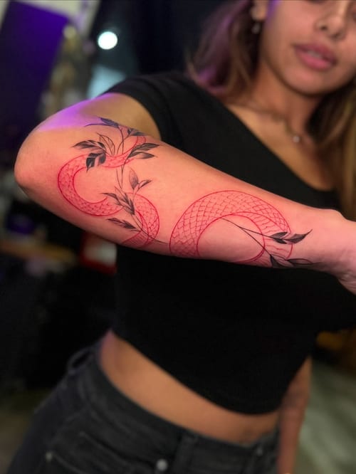 A minimal linework tattoo of a snake intertwined with leaves on the forearm, using red and black ink — by zealous, los angeles