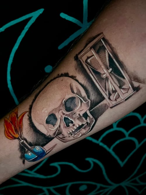 A realistic skull and hourglass tattoo on the forearm, featuring black and grey shading with a touch of color in the flame and liquid elements — by Josue Bravo, los angeles