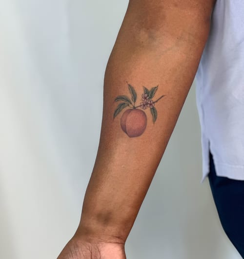 A delicate color tattoo of a peach with leaves and flowers on the forearm, done in a fine line botanical style — by Melanie Benoit, los angeles