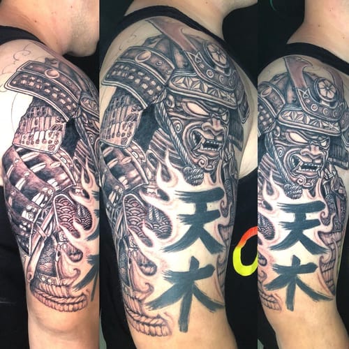 A bold black and grey samurai warrior tattoo on the upper arm, featuring detailed armor and script elements — by Sandra Price, los angeles