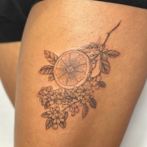 A delicate black and grey tattoo of an orange slice with flowers on the thigh, featuring fine line botanical details — by Melanie Benoit, los angeles