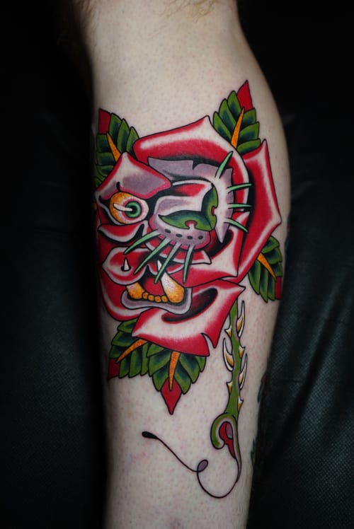 A colorful Neo-Traditional tattoo on the calf featuring a skull integrated into a vibrant red rose with green leaves — by Megan Rose, los angeles