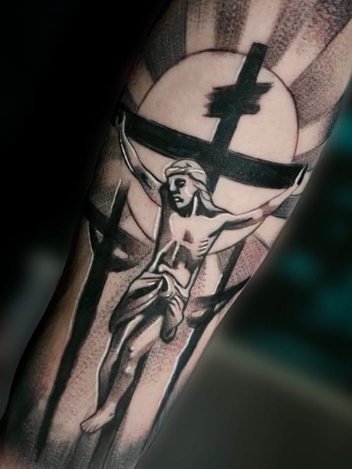 A black and grey tattoo of Jesus on the cross with dotwork shading on the forearm, featuring strong black lines and a halo effect — by Josue Bravo, los angeles