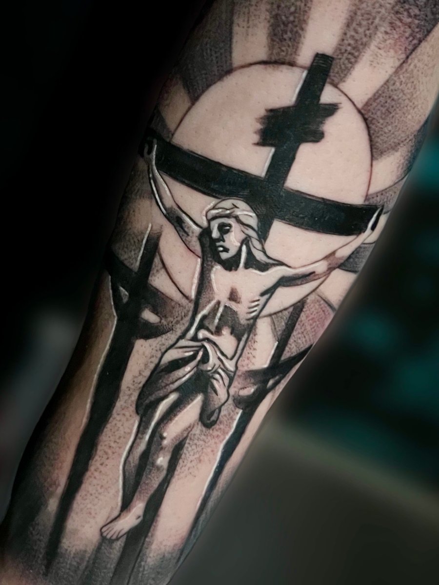 A black and grey tattoo of Jesus on the cross with dotwork shading on the forearm, featuring strong black lines and a halo effect — by Josue Bravo, los angeles