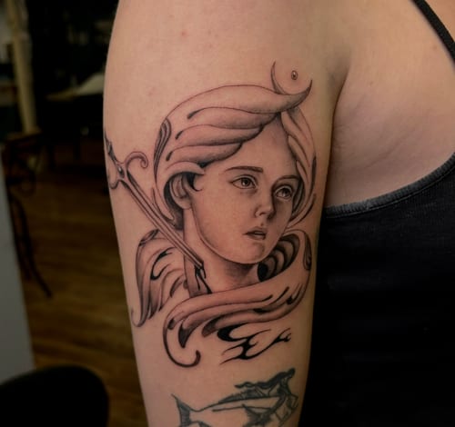 A black and grey neo-traditional tattoo of a woman's face on the upper arm, featuring flowing hair and soft shading — by velvet devil, los angeles