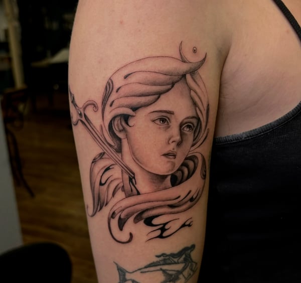 A black and grey neo-traditional tattoo of a woman's face on the upper arm, featuring flowing hair and soft shading — by velvet devil, los angeles