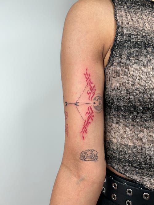 fine line bow and arrow wrapped in flowing red flame accents on the upper arm — by brian kies, los angeles