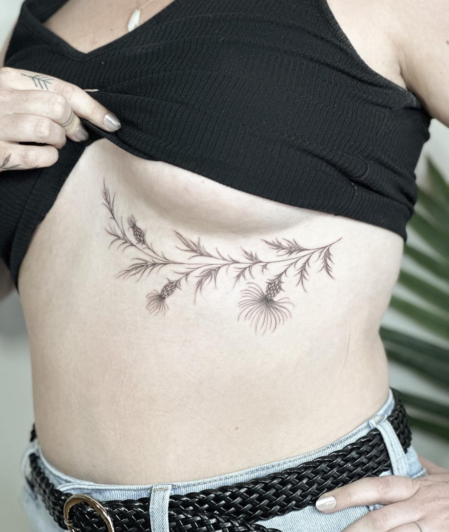 A delicate black and grey fine line botanical branch tattoo on the rib, featuring intricate floral details — by Melanie Benoit, los angeles