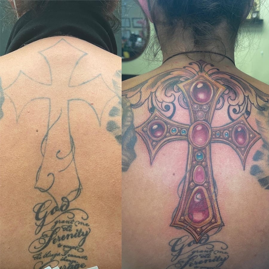 An ornate and colorful cross tattoo on the back with detailed embellishments and script lettering below — by Sandra Price, los angeles