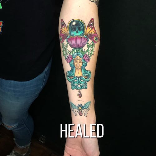 A colorful neo-traditional tattoo on the forearm featuring a woman's face surrounded by floral and insect elements — by Sandra Price, los angeles