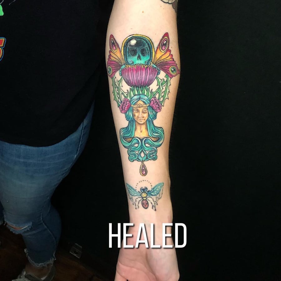 A colorful neo-traditional tattoo on the forearm featuring a woman's face surrounded by floral and insect elements — by Sandra Price, los angeles