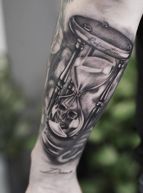 A black and grey realism tattoo of an hourglass with a skull inside, located on the forearm with detailed shading — by Jian Liang, los angeles