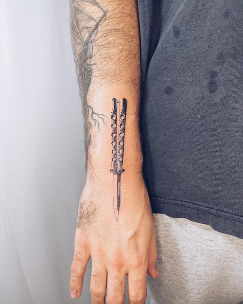 A minimal blackwork dagger tattoo on the hand, featuring a simple and clean design — by Level tattoo, los angeles