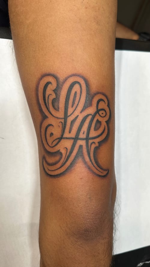 A black and grey lettering tattoo on the arm featuring stylized script with bold outlines and shading — by Humilde tattoos, los angeles