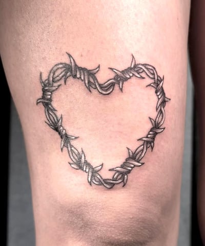 A minimalist black and grey tattoo of a heart made from barbed wire on the leg — by Shelby Bianco, los angeles