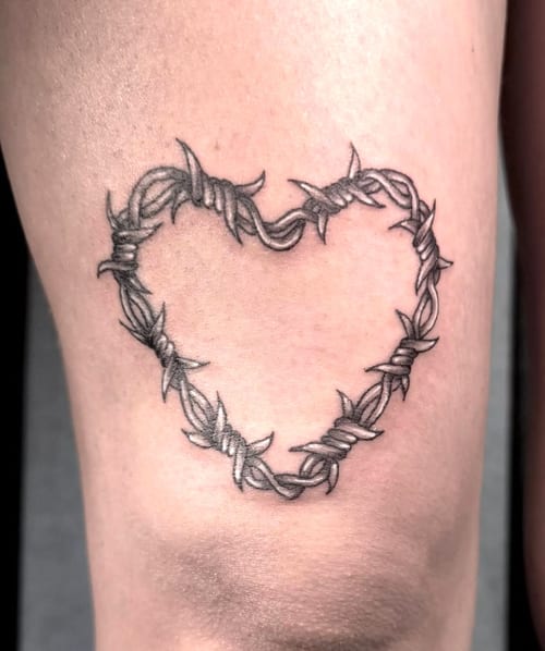 A minimalist black and grey tattoo of a heart made from barbed wire on the leg — by Shelby Bianco, los angeles