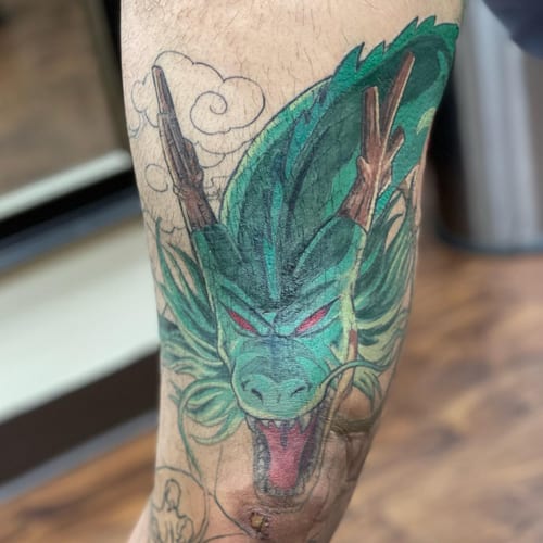 A bold and colorful Japanese-style dragon tattoo on the arm, featuring vibrant green and red hues — by Sandra Price, los angeles