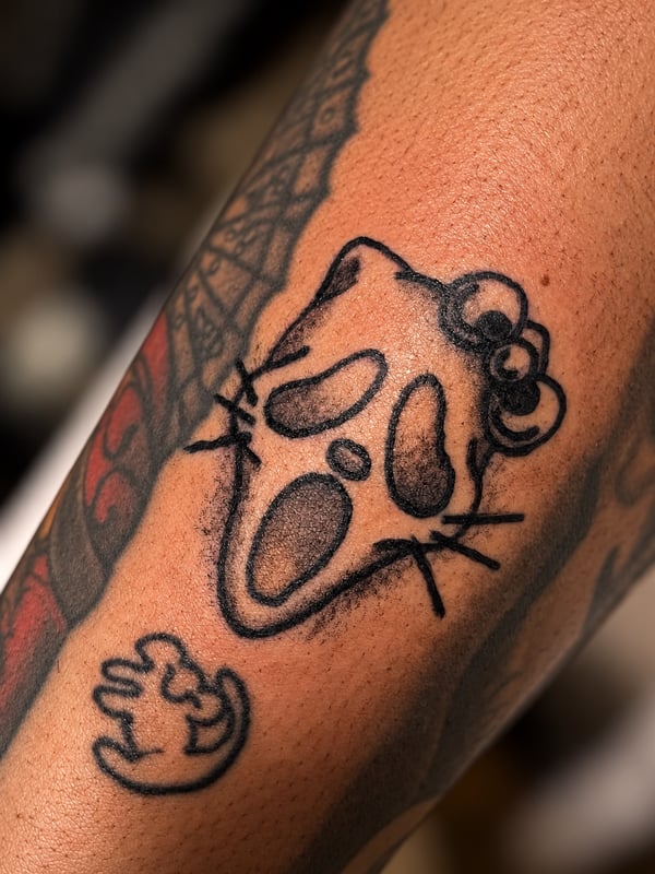 A whimsical black and grey cartoon cat face tattoo on the arm, featuring minimalist linework — by HEAVY INK, chino, ca