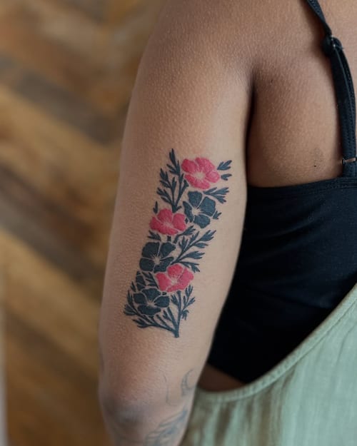 A bold traditional floral bouquet tattoo on the upper arm with vibrant red flowers and dark leaves — by Dylan Aiello, los angeles