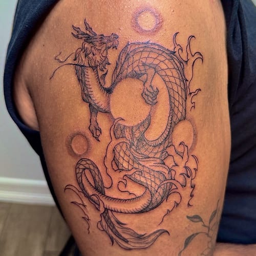 A bold black and grey linework dragon tattoo on the upper arm, featuring intricate Japanese style details — by NJ TATTOOZ, los angeles