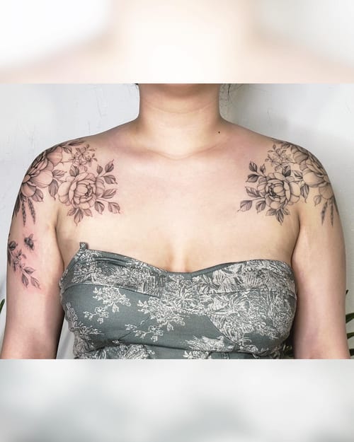 A delicate black and grey floral arrangement tattoo on the shoulders featuring fine line work and clean detailing — by Melanie Benoit, los angeles