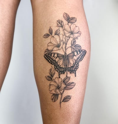 A delicate black and grey butterfly and floral tattoo on the calf, featuring fine line details and clean shading — by Melanie Benoit, los angeles