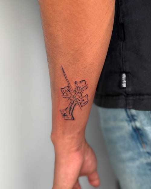 A minimal black linework cross tattoo on the forearm with a simple and clean design — by zealous, los angeles
