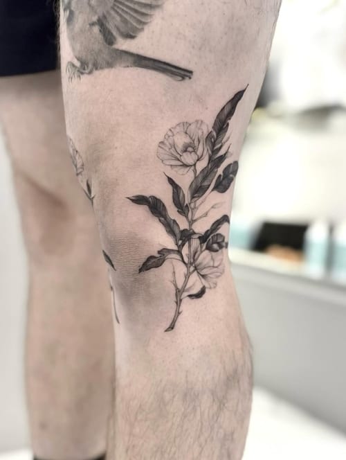 A black and grey botanical tattoo on the thigh featuring detailed flowers and part of a bird in flight — by otaybeatdown, los angeles