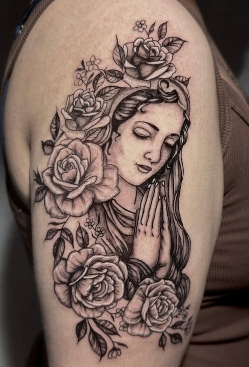 A black and grey realism tattoo of the Virgin Mary surrounded by roses on the upper arm, featuring detailed shading and fine line work — by Shelby Bianco, los angeles