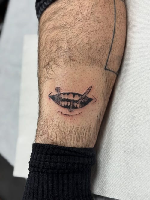 A black and grey tattoo of a mouth with nails on the forearm, done in a minimalist blackwork style — by Sandra Price, los angeles