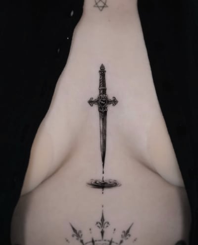 A fine line black and grey tattoo of a dagger on the sternum, featuring intricate details and a reflection effect below the blade — by Jian Liang, los angeles