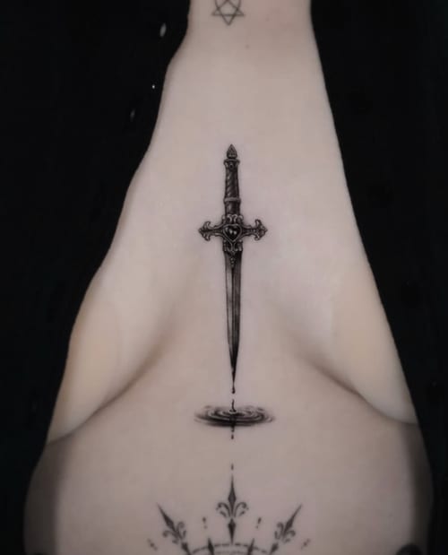 A fine line black and grey tattoo of a dagger on the sternum, featuring intricate details and a reflection effect below the blade — by Jian Liang, los angeles