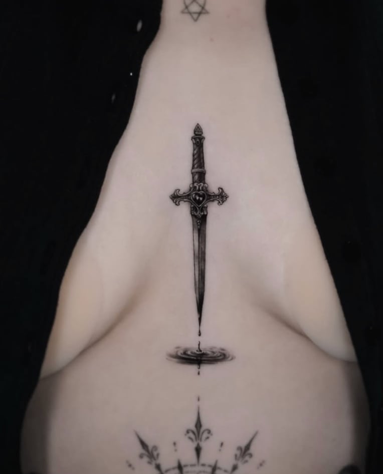 A fine line black and grey tattoo of a dagger on the sternum, featuring intricate details and a reflection effect below the blade — by Jian Liang, los angeles