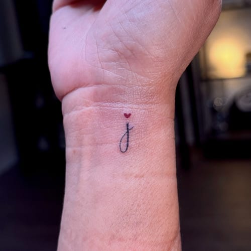A minimalist tattoo of the letter 'j' with a small red heart above it on the wrist — by NJ TATTOOZ, los angeles