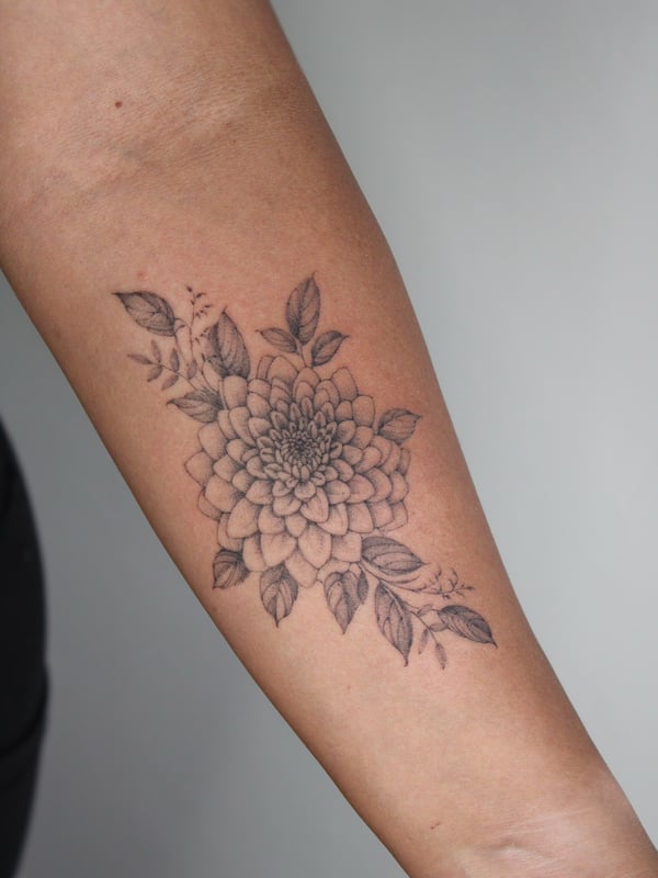A delicate black and grey fine line flower tattoo on the forearm, featuring detailed petals and leaves — by Melanie Benoit, los angeles