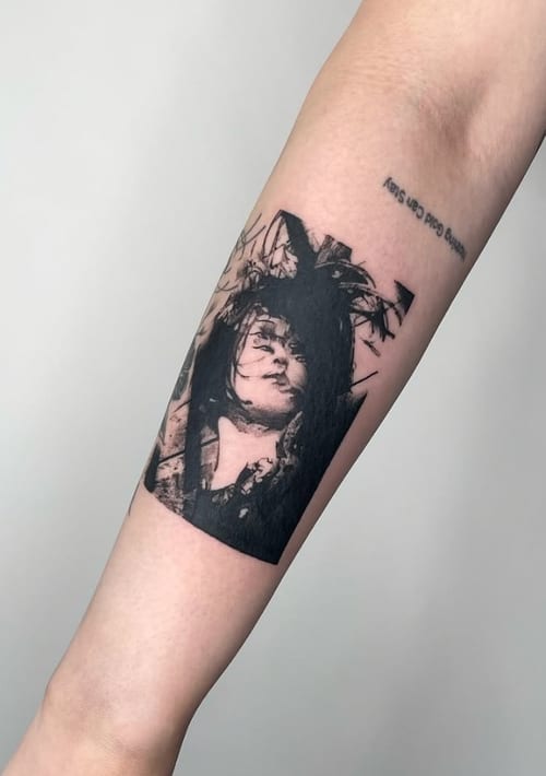 A black and grey portrait tattoo on the forearm, featuring a detailed face with a dark, abstract background — by Level tattoo, los angeles
