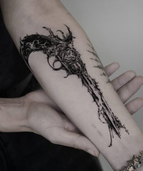 A black and grey illustrative tattoo of an ornate gun on the forearm with intricate detailing and bold lines — by Jian Liang, los angeles