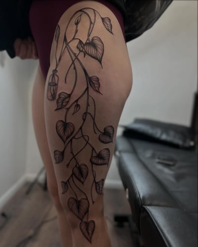 A delicate blackwork tattoo of a vine with heart-shaped leaves on the thigh — by Maddie Ramirez, los angeles