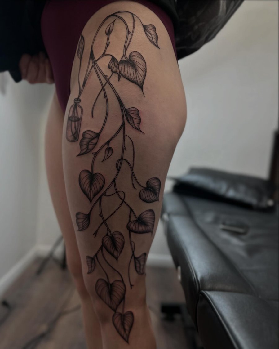 A delicate blackwork tattoo of a vine with heart-shaped leaves on the thigh — by Maddie Ramirez, los angeles