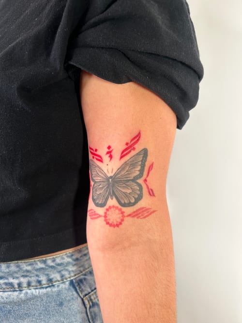 black and grey butterfly framed by red ornamental accents and a starburst above the elbow — by brian kies, los angeles