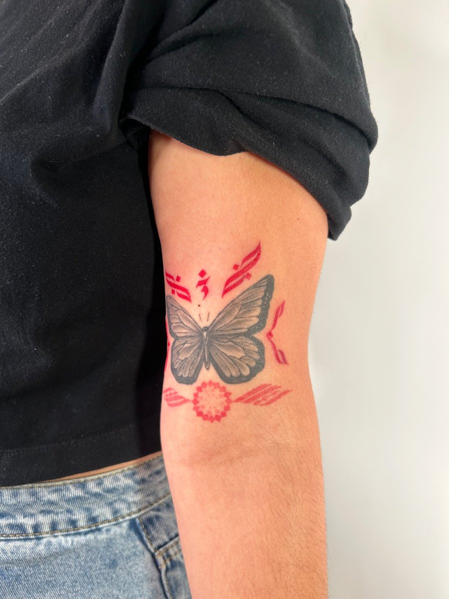 A mixed color tattoo of a butterfly with red decorative elements on the upper arm, featuring bold outlines and illustrative style — by Brian Kies, los angeles