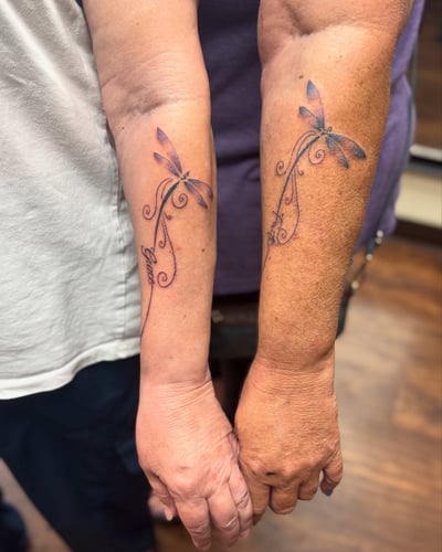 Matching delicate dragonfly tattoos with fine line script on the forearm, featuring a minimalist design in color — by Sandra Price, los angeles