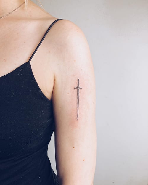 A minimalist black and grey sword tattoo on the upper arm with clean linework — by Level tattoo, los angeles