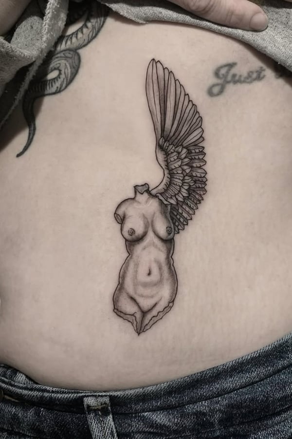 A black and grey fine line tattoo of a winged female torso on the stomach, featuring detailed line work and shading — by Shelby Bianco, ventura, ca