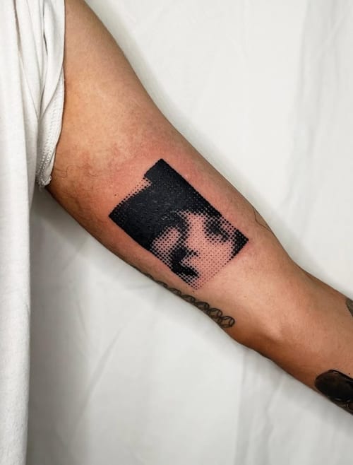 A black and grey dotwork portrait tattoo on the inner arm, featuring a stylized face with bold black areas and dotted shading — by Level tattoo, los angeles