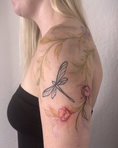 A delicate watercolor tattoo of a dragonfly and flowers on the shoulder, featuring fine line details and soft colors — by Melanie Benoit, los angeles