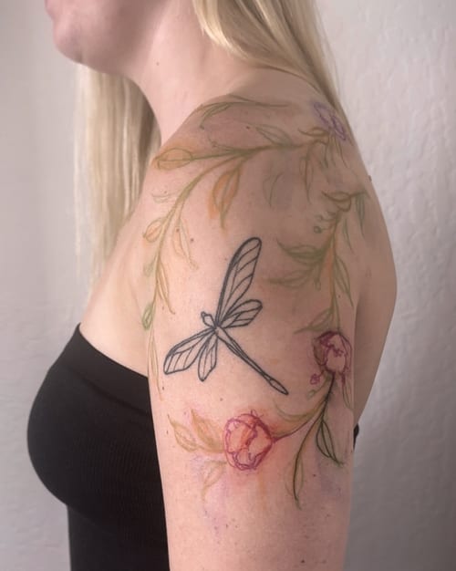 A delicate watercolor tattoo of a dragonfly and flowers on the shoulder, featuring fine line details and soft colors — by Melanie Benoit, los angeles