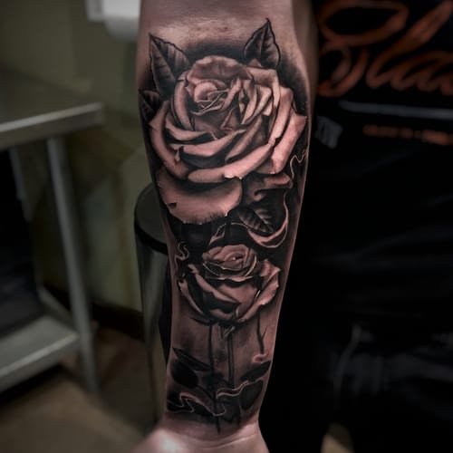 A black and grey realism tattoo of two roses on the forearm with detailed shading and depth — by Travis Ross, los angeles