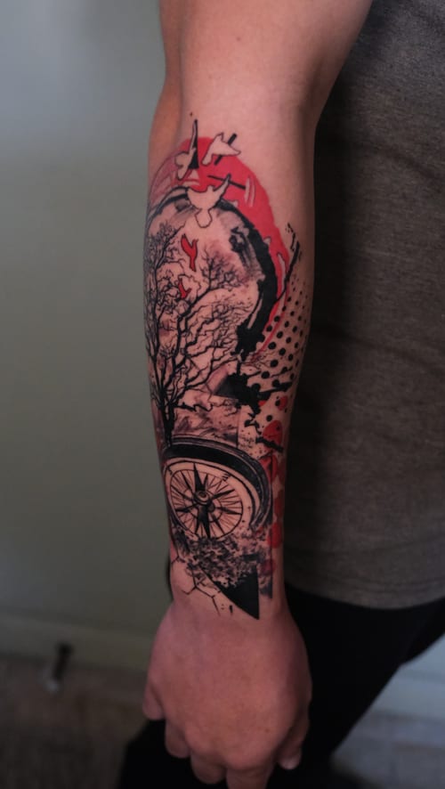 A Trash Polka style tattoo on the forearm featuring a tree and compass with abstract elements in black and red ink — by Nik Lucas, los angeles